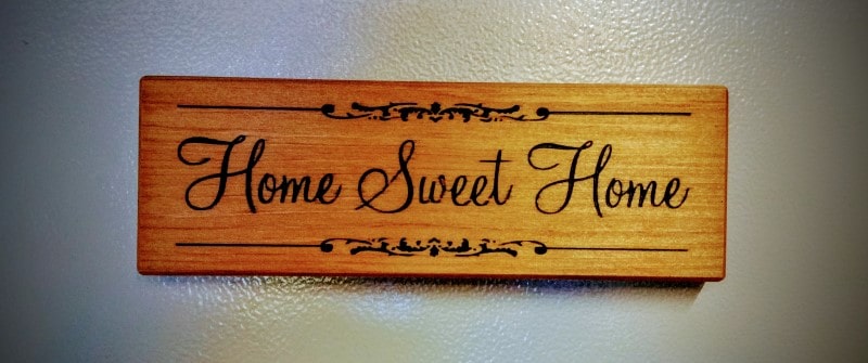 Front view of a small engraved wooden quote reads home sweet home. Magnetic