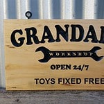 Pine sign with carved black engraved lettering and black screw eyes for easy hanging. Reads 'Granddad's workshop open 24/7 toys fixed free'