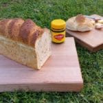 chopping boards on green grass with a loaf of bread and vegemite spread kabana and cheese with knife