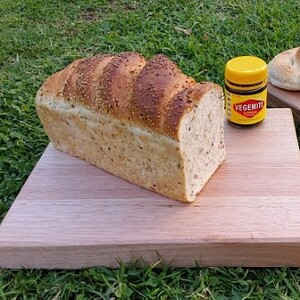 chopping boards on green grass with a loaf of bread and vegemite spread kabana and cheese with knife