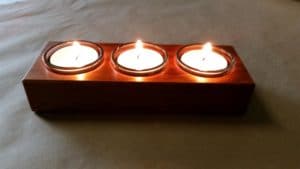 closeup of tealight candle holders in use showing the reflections of lit flame off the timber surface