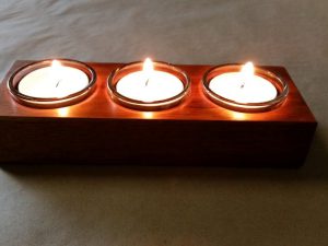 closeup of tealight candle holders in use showing the reflections of lit flame off the timber surface