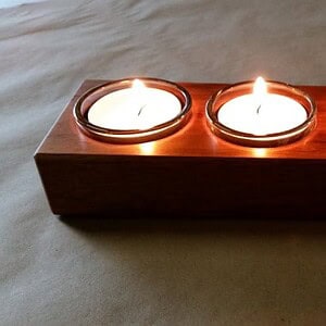 closeup of tealight candle holders in use showing the reflections of lit flame off the timber surface