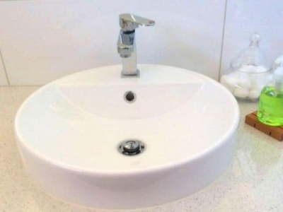 A wooden soap holder with a pump soap bottle on top sitting next to a modern bathroom sink