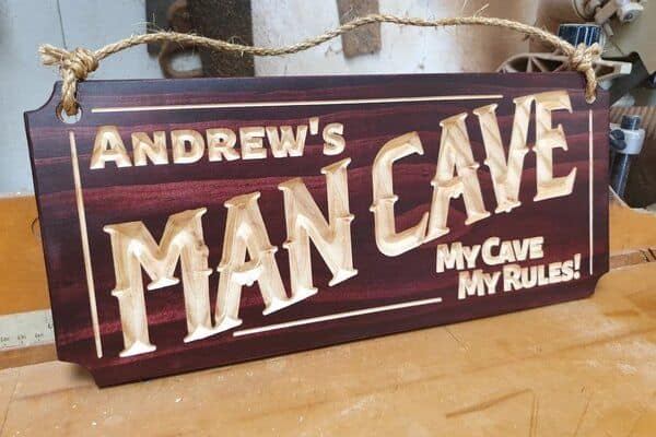 An example of a personalised mancave sign saying 'Andrew's MANCAVE MY CAVE MY RULES' featuring English Mahogany stain and rustic hanging rope.