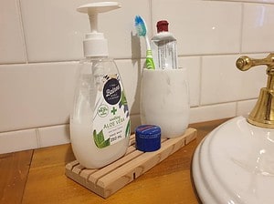 Longer length wooden soap holder being used in a bathroom to hold pump soap bottle, toothpaste and toothbrush holder