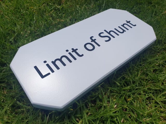 white painted wooden sign in the classic railway sign shape laying on the grass with the words 'Limit of Shunt' engraved and painted black