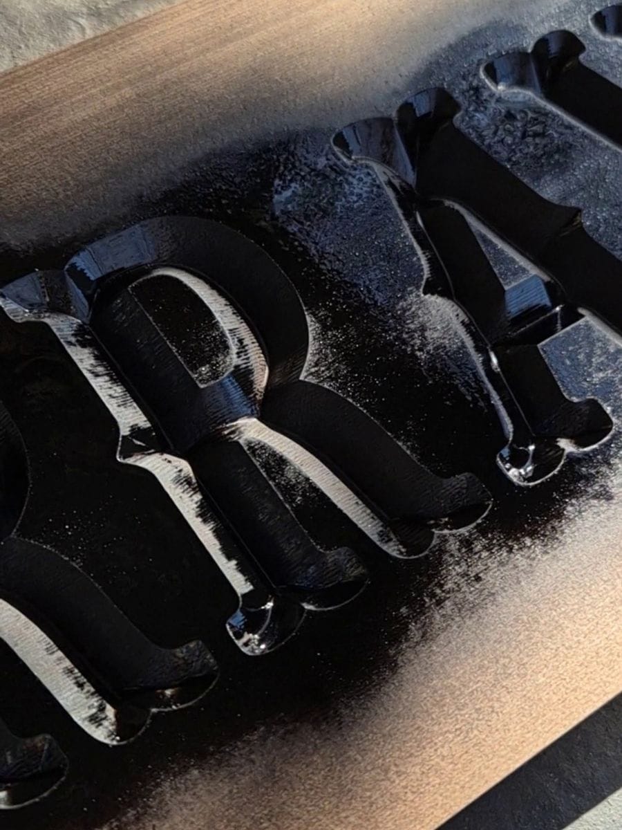 Close-up of freshly painted black carved lettering on a wooden sign drying before sanding.