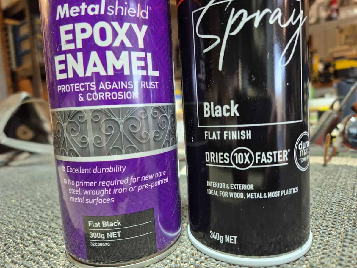 Two cans of flat black spray paint used for painting carved lettering on wooden signs.