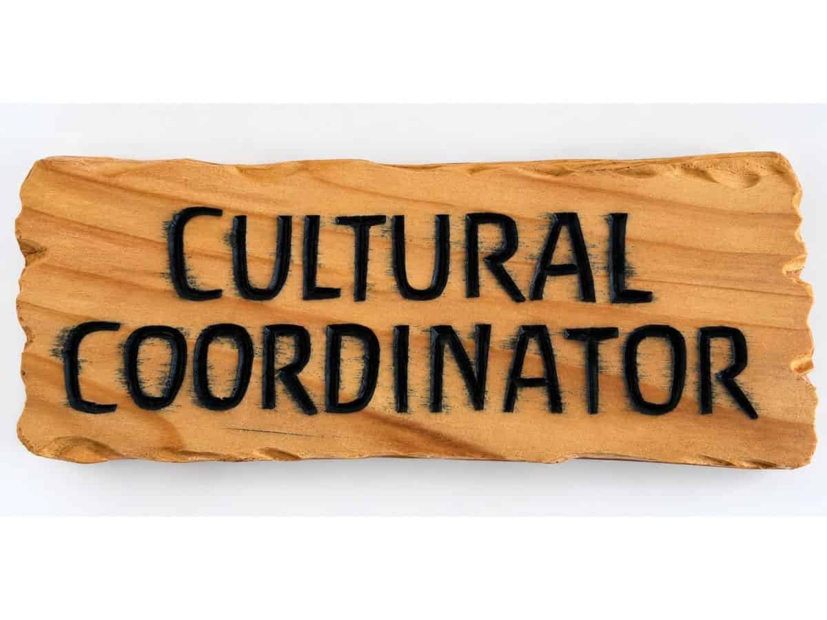 Cedar wooden sign with black paint bleeding into the timber grain around the carved Cultural Coordinator lettering.