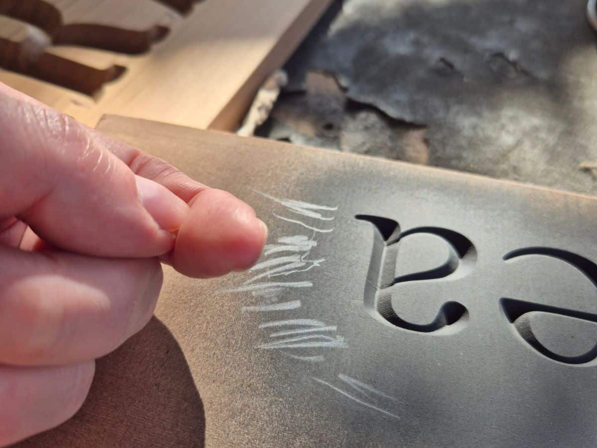 Checking a fingernail for black paint after testing whether spray paint on a wooden sign is dry.