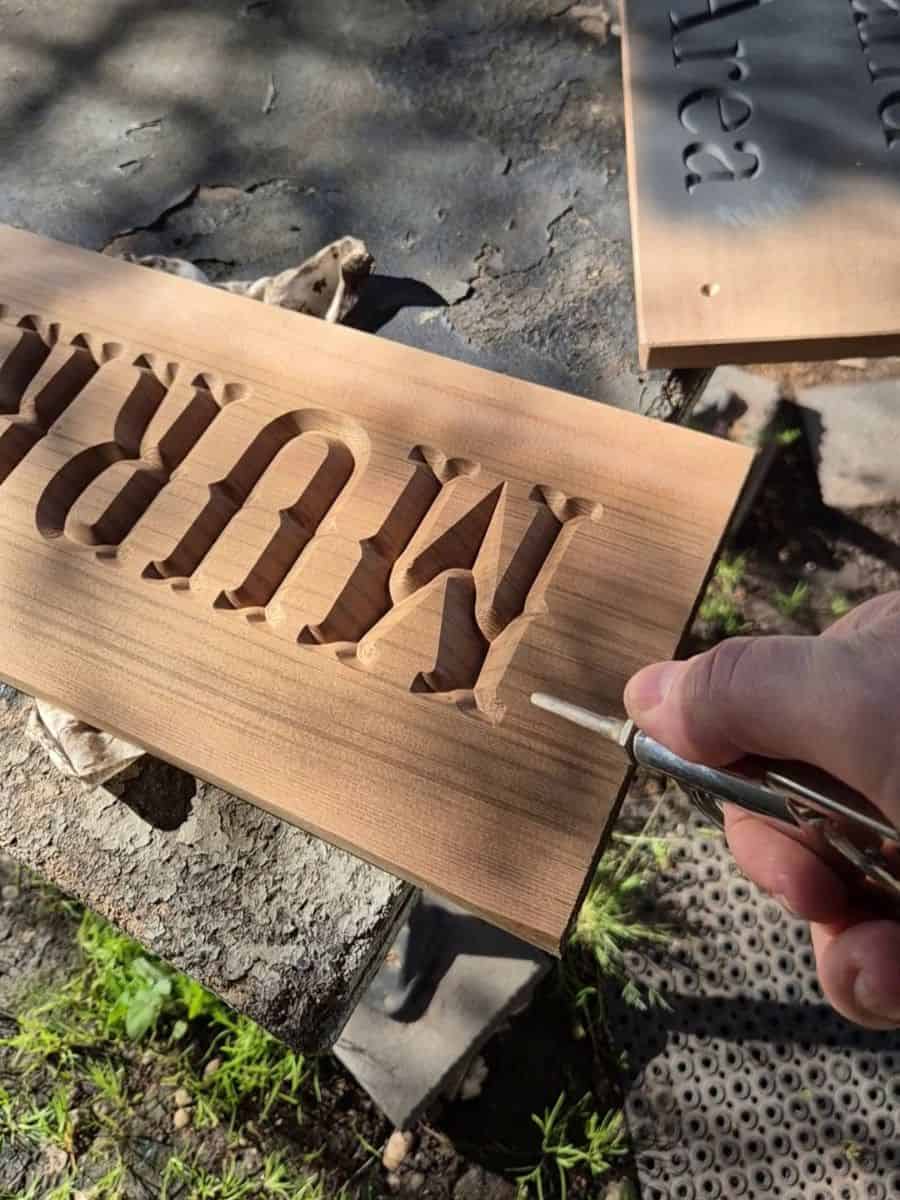 Using compressed air to blow dust and loose wood fibres from carved wooden sign lettering before painting.