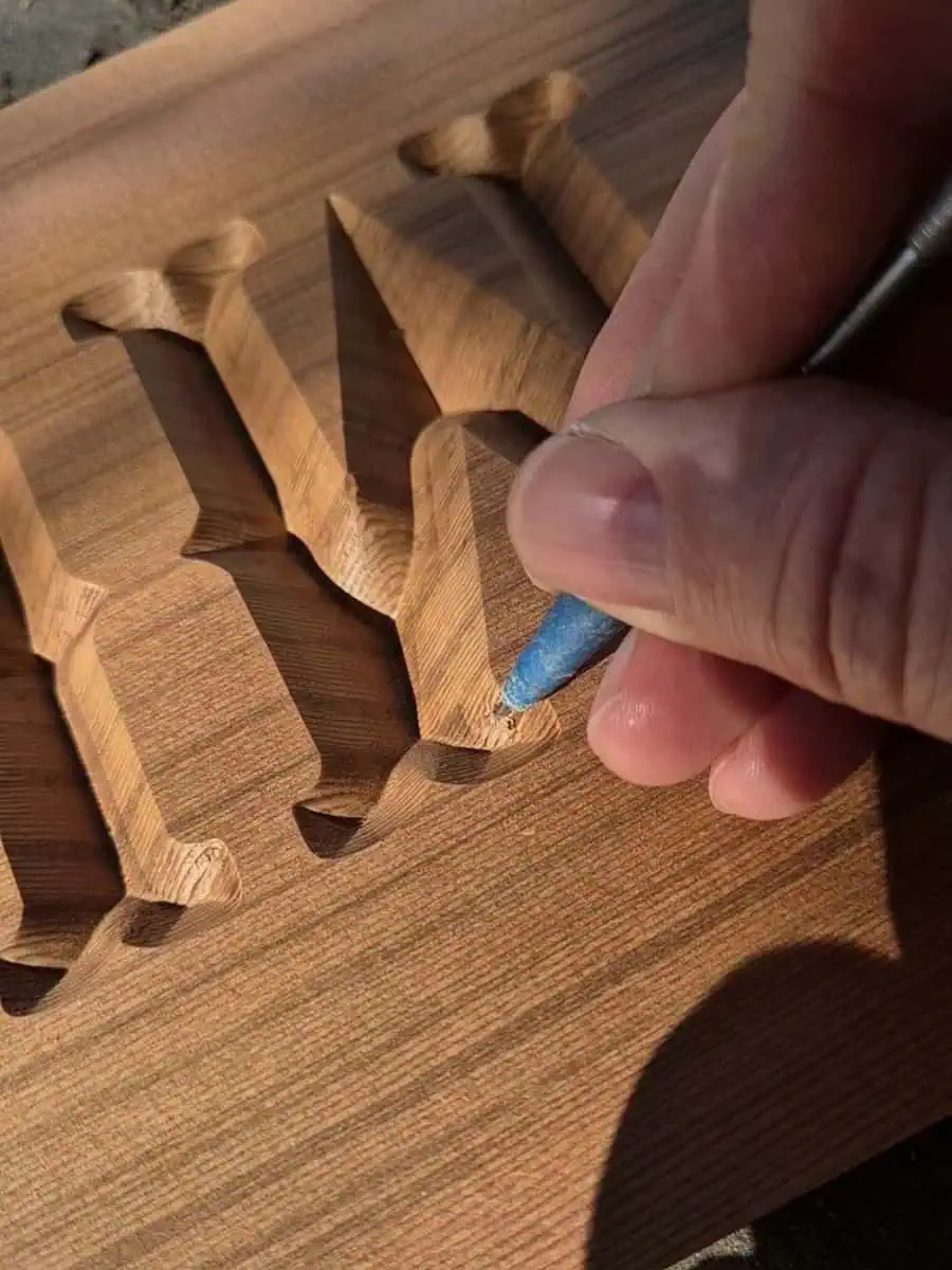 Using a small scribe to remove burrs and loose wood fibres from carved wooden sign lettering before painting.