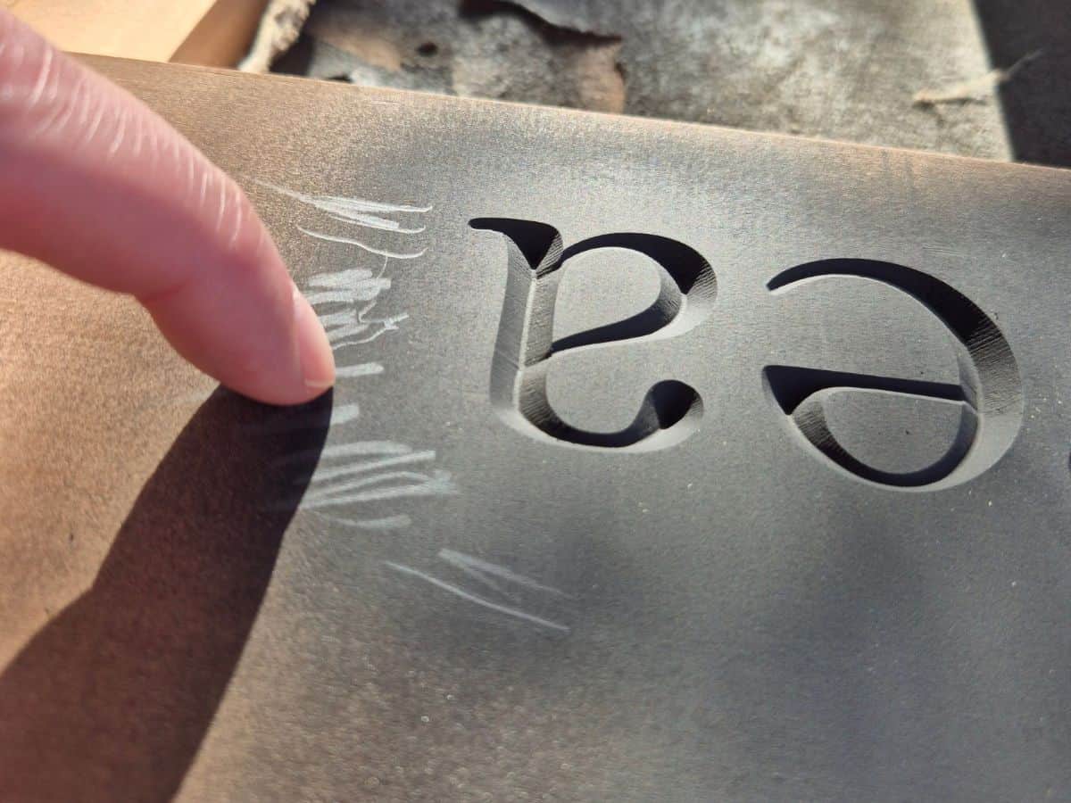 Testing black spray paint on a wooden sign with a fingernail to check whether the paint is dry enough for sanding.