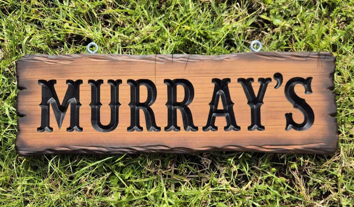 Finished rustic timber sign reading Murray’s with carved black painted lettering and scorched edges.