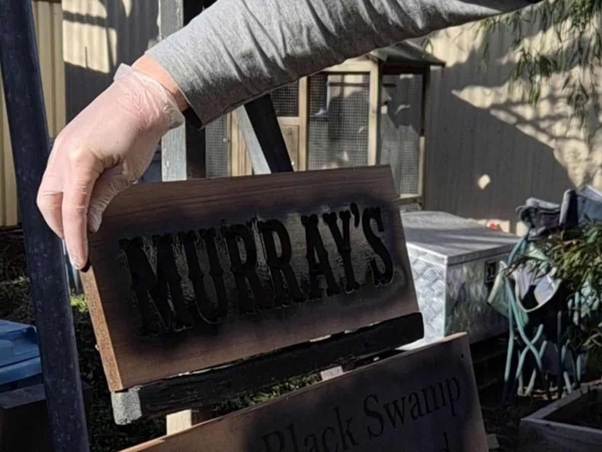 Turning a carved wooden sign between coats of black spray paint to cover the lettering from different directions.