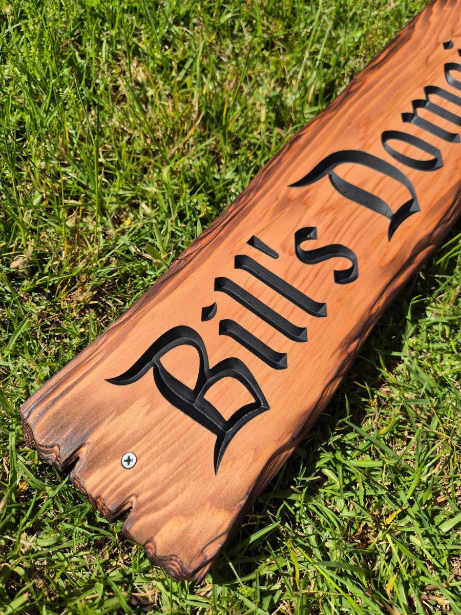 Rustic timber sign with carved matt black lettering, scorched edges and a natural wood finish.
