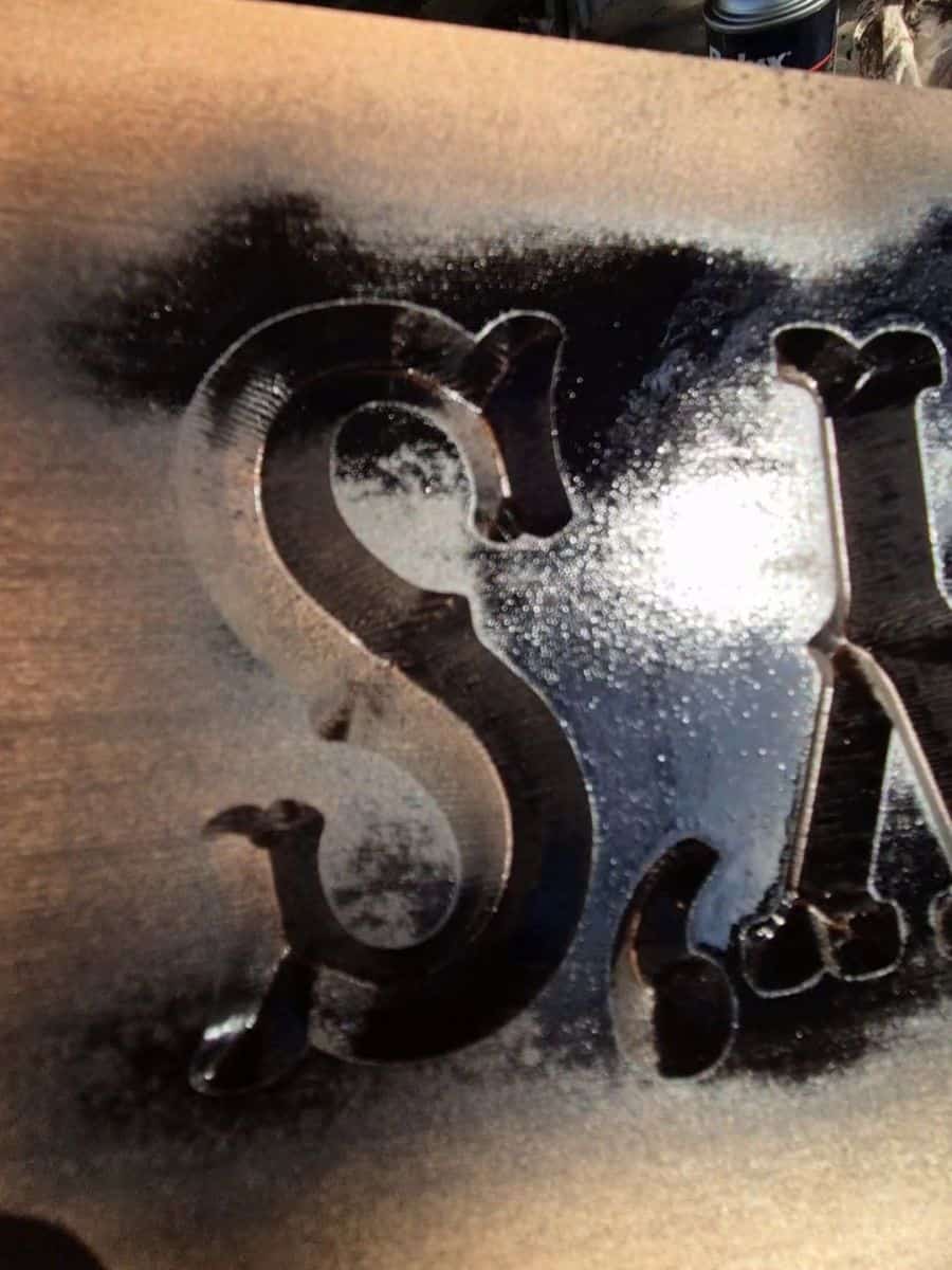 Close-up of wet black spray paint running down across carved lettering on a wooden sign.