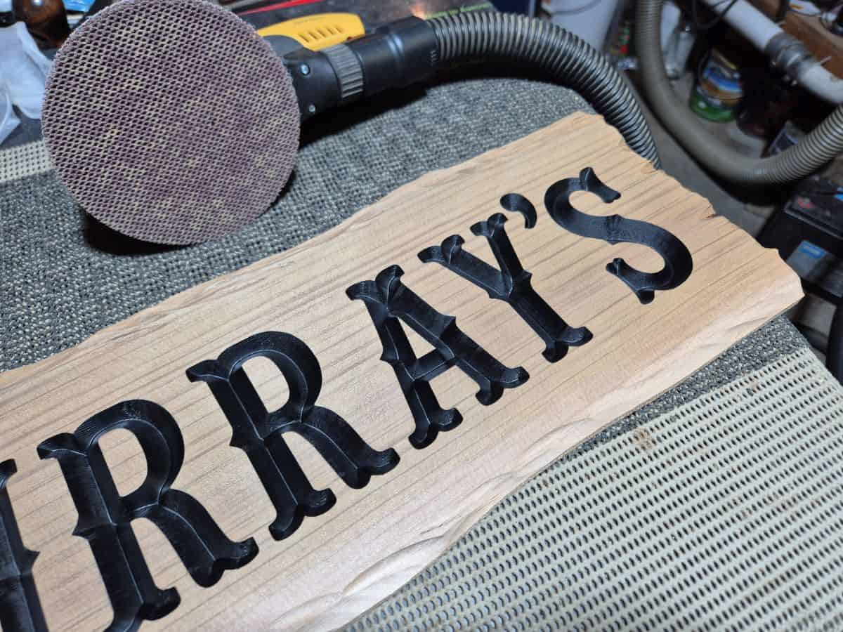 Close-up of black painted carved lettering after the wooden sign surface has been sanded clean.