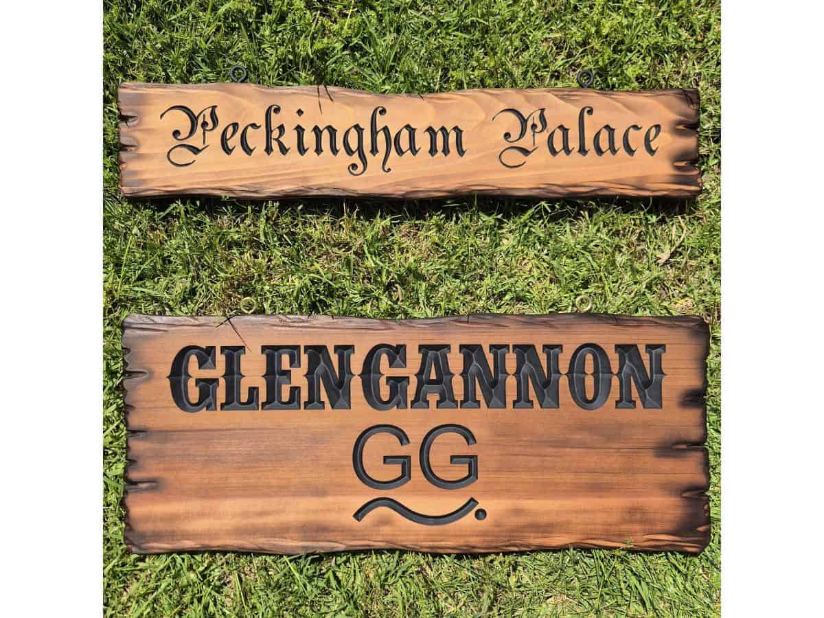 Two rustic timber signs with carved matt black lettering, scorched edges and different lettering styles laying on the grass in my backyard.