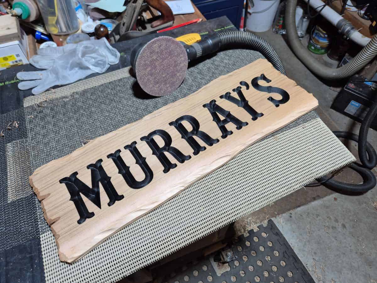 Wooden sign after sanding away the black overspray, leaving clean timber and black painted carved lettering.