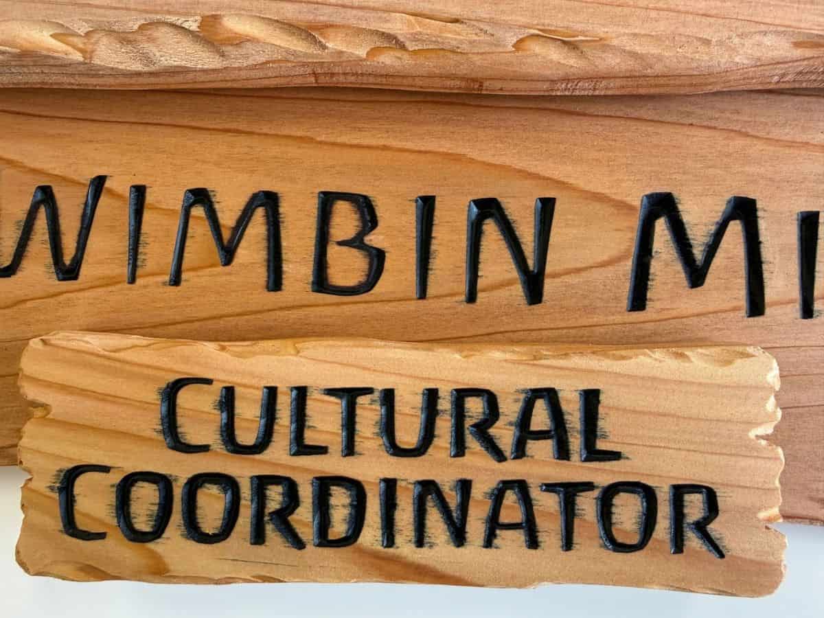 Black paint bleeding into the timber grain around carved lettering on wooden cedar signs.