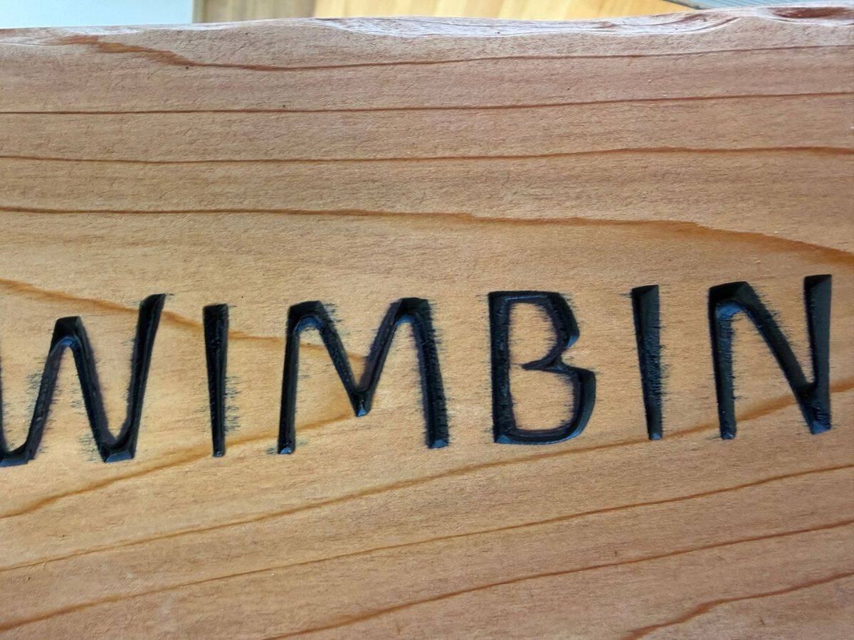 Black paint bleeding into the timber grain around carved lettering on a wooden sign